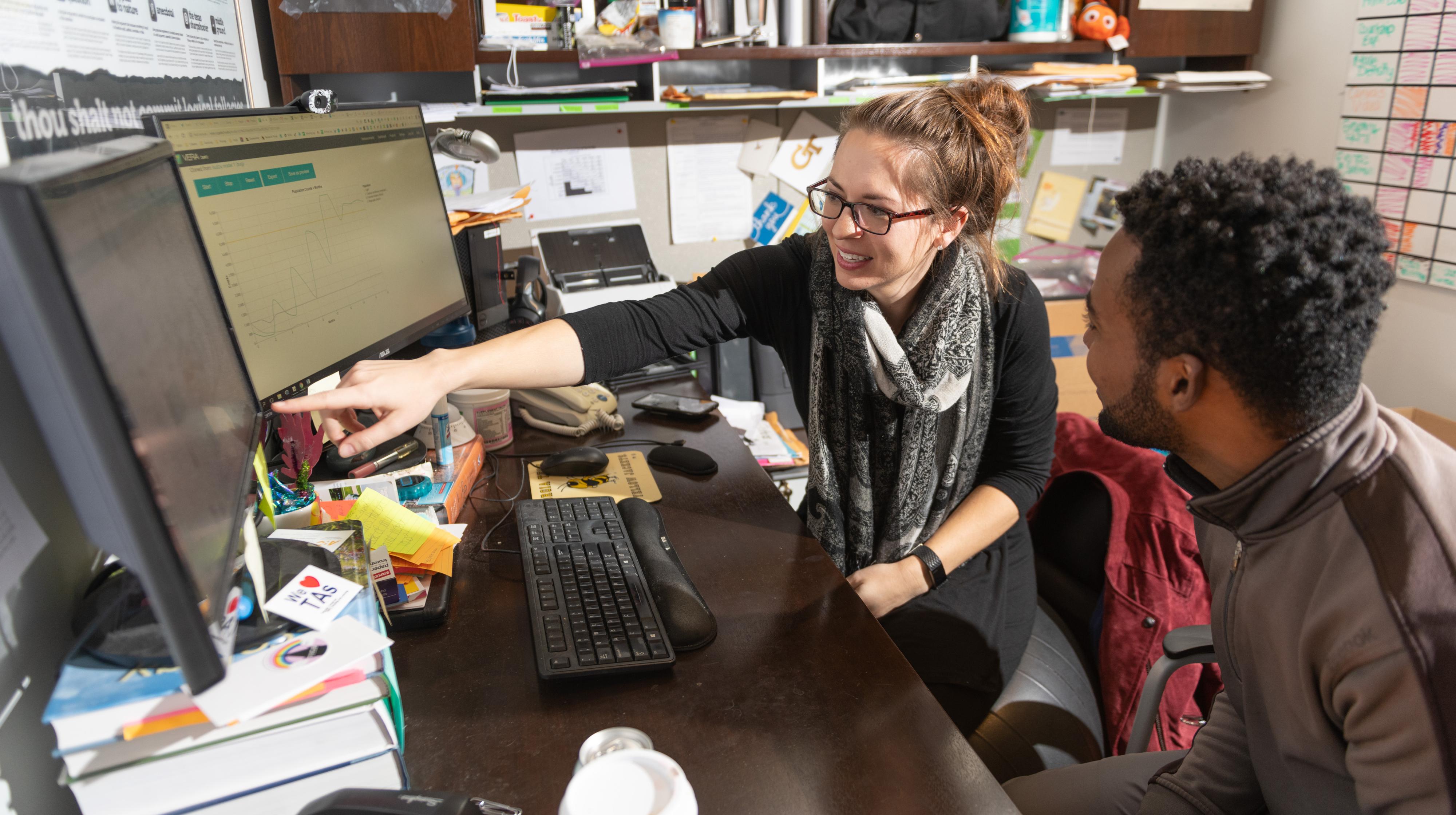 A teacher shares her thoughts with a student by pointing to a project on a computer screen